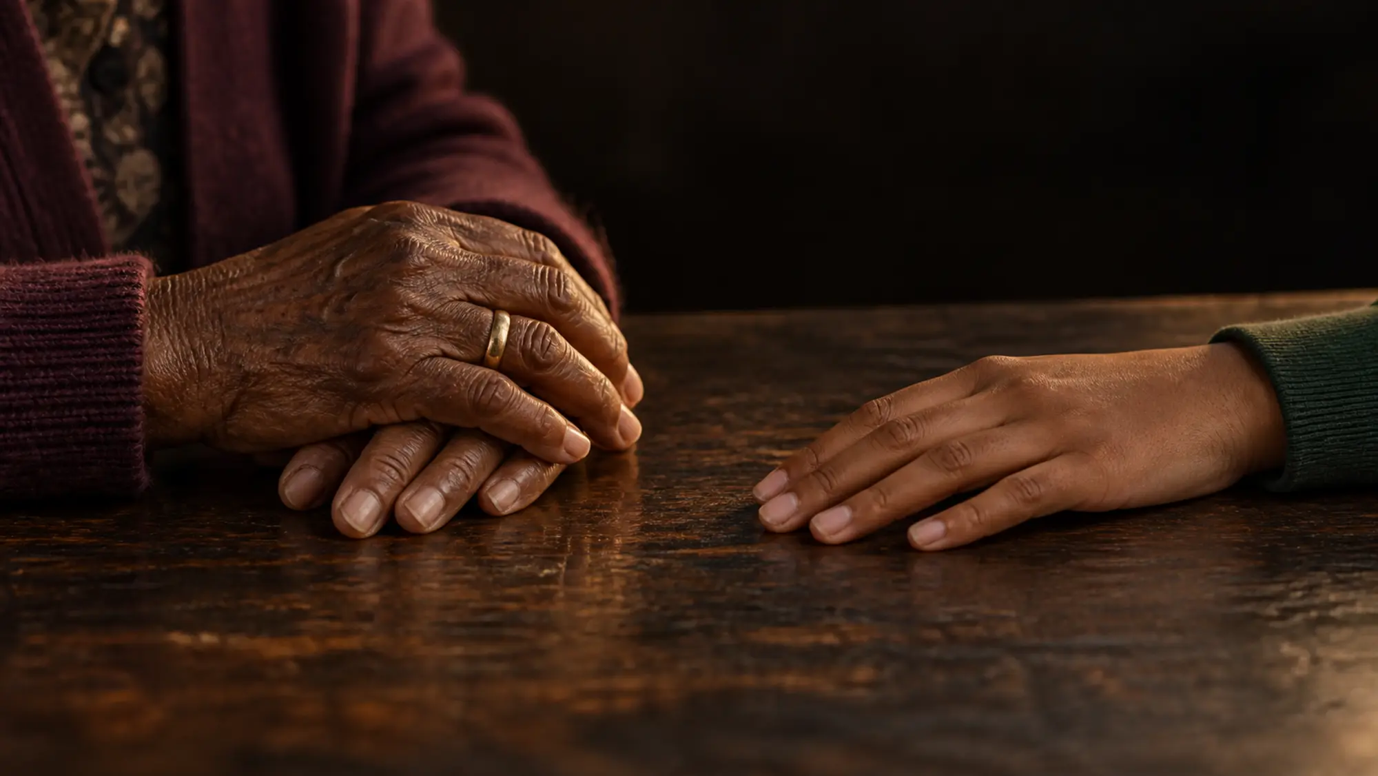 An older hand resting beside a younger one on a worn wooden table